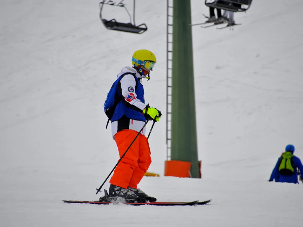 Skifahrer in oranger Hose fährt an der Liftstütze vorbei.